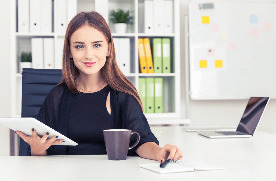 Eine junge Personaldienstleistungskauffrau mit einem Tablet und einem Notizbuch in der Hand, die lächelnd in ihrem Büro sitzt: