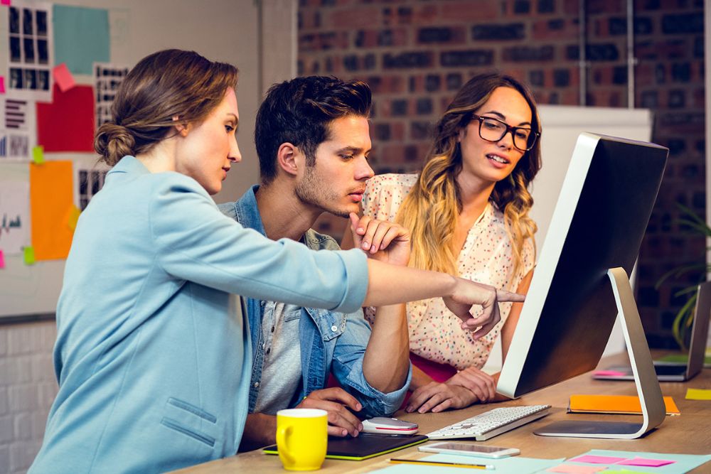 Drei Mitarbeitende vor dem Bildschirm im Büro beim Demonstrieren der Vertriebssoftware