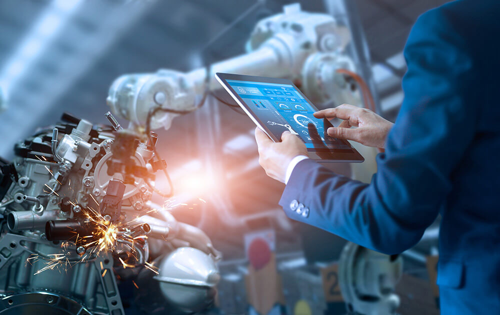 Industrielle Automation und Technologie Eine Person in einem Business Anzug verwendet ein Tablet, um einen automatisierten Prozess in der Fertigungsindustrie zu steuern, was auf einen der beliebten Berufe im Bereich der industriellen Automation hinweist. Im Hintergrund führt ein Roboterarm Schweißarbeiten an einem Maschinenteil aus, wobei Funken sprühen. Die moderne Technologie steht im Kontrast zu der menschlichen Interaktion mit der Maschinerie, was die fortschrittliche Natur dieser Berufsfelder unterstreicht