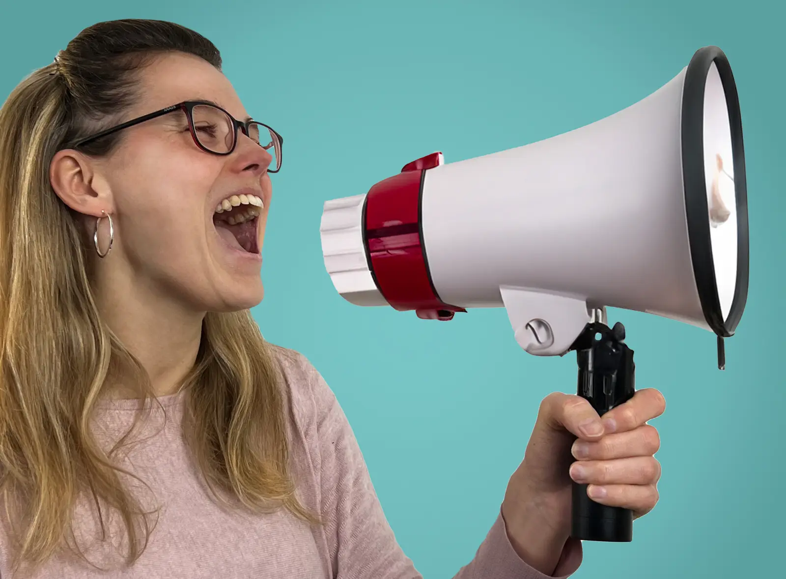 frau-mit-megafon-verkündet-botschaft Eine Frau mit langen, blonden Haaren und Brille hält ein Megafon in der Hand und spricht laut hinein. Sie trägt einen rosa Pullover und lächelt leicht, während sie ihre Botschaft durch das Megafon verbreitet. Der Hintergrund ist einfarbig in einem hellen Türkis gehalten.
