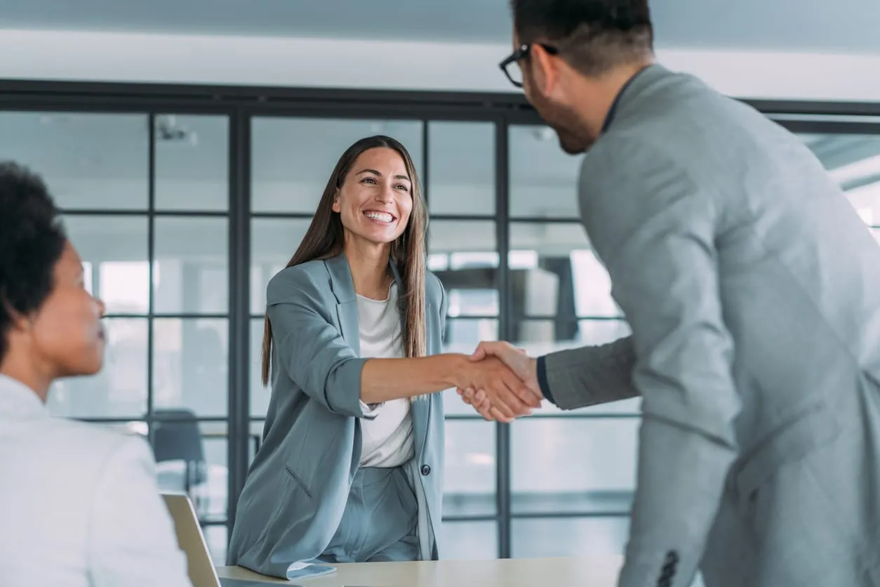 Erfolgreiche Wiedereinstellung und Teamintegration Freudige Wiedereinstellung: Ein Geschäftsmann begrüßt eine ehemalige Mitarbeiterin mit einem Handschlag im Büro, während eine Kollegin zustimmend zusieht.